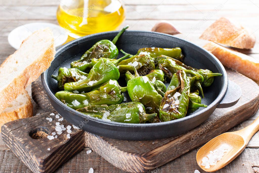 Authentic Spanish padron peppers with salt and olive oil on frying pan on a wooden table