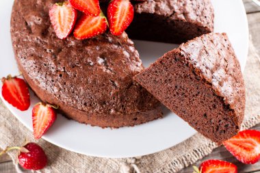 Yuvarlak fırında çikolatalı kek ve ahşap masada çilek.