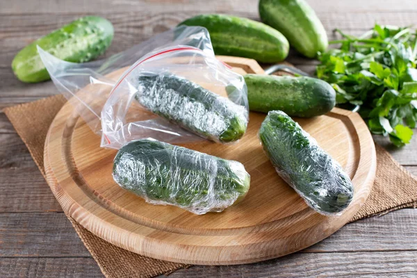Fresh green cucumbers in cling film on a cutting board on a wooden table. Frozen whole cucumbers. Frozen Food Concept.