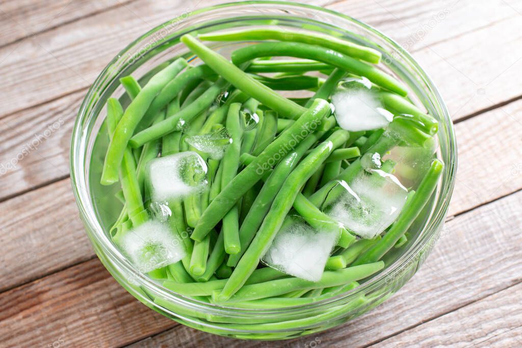 Boiled vegetables, green beans in ice water after blanching on a wooden table