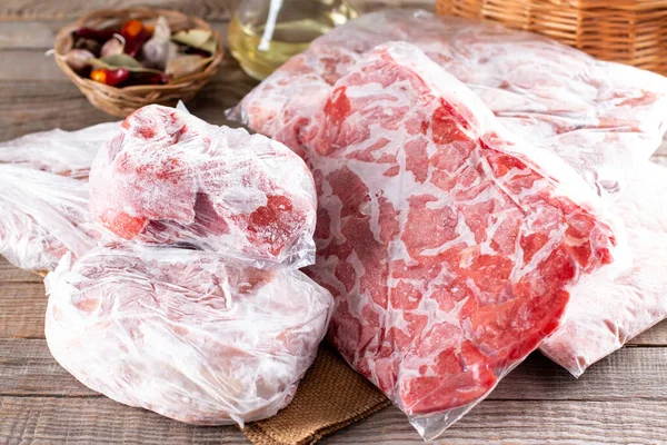 Frozen meat in a plastic bag on a wooden table. Frozen food.