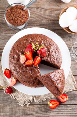 Yuvarlak fırında çikolatalı kek ve ahşap masada çilek.