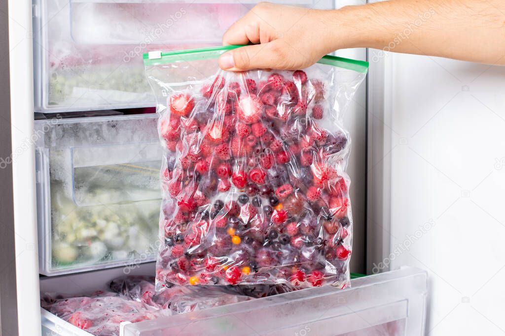 Frozen berries in transparent plastic bags in the freezer. Open deep freeze filled with frozen berries. Concept of healthy eating. Frozen food.