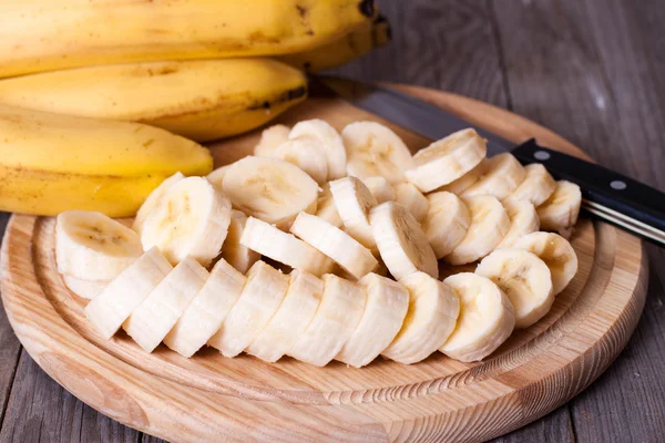 Bananes et tranches de banane sur une planche de bois — Photo