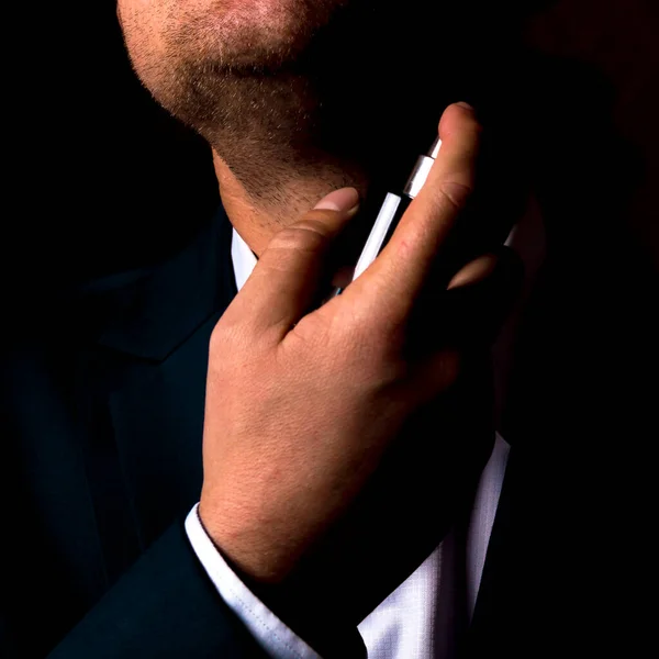 Man in a business suit with a bottle of perfume on a black background.Preparing for a business meeting.
