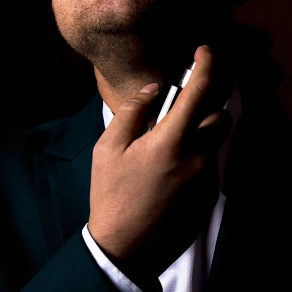 Man in a business suit with a bottle of perfume on a black background.Preparing for a business meeting.