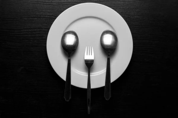 勺子和叉子放在白色圆盘上 模仿用餐具做的脸的模仿 深色木制背景 — 图库照片
