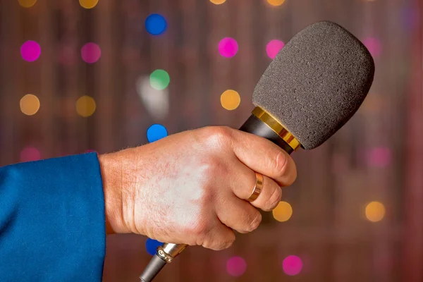 Microphone in hand. Interview. Karaoke. A man\'s hand holds a microphone against the background of blurry garlands