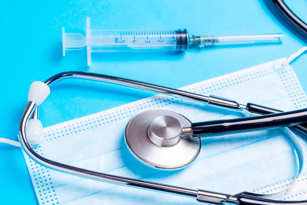 Stetoskop, koruyucu maske ve mavi arka planda şırınga. Doktor aletleri..