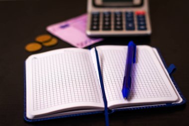 Kalem, not defteri, para ve karanlık bir arka planda hesap makinesi. Muhasebe, gider ve gelir planlaması.