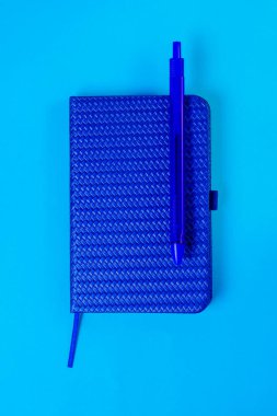 Mavi arka planda tükenmez kalem ve not defteri. Tek renkli mavi renk paleti. Kırtasiye.