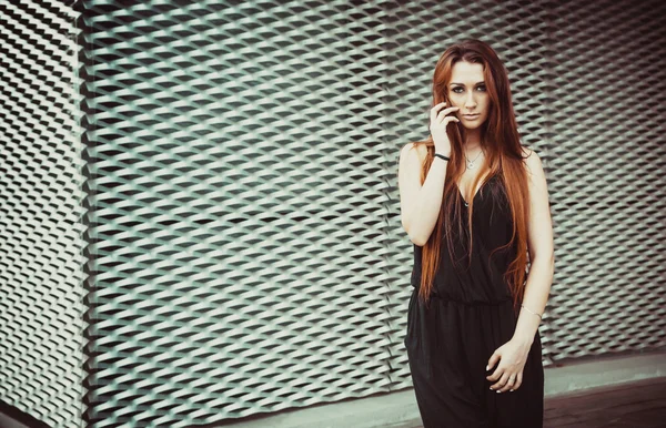 Red-haired girl model stands near wall in a modern architectural style