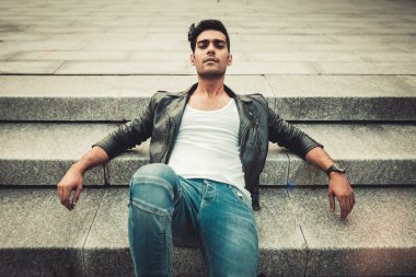Beyaz T-shirt, deri ceket ve kot basamaklarında oturan poz şık adam.