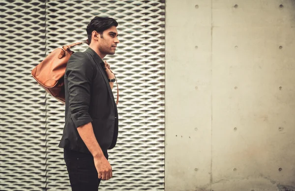 Stylish model looking man profile with handbag on his shoulder in modern architectural environment.