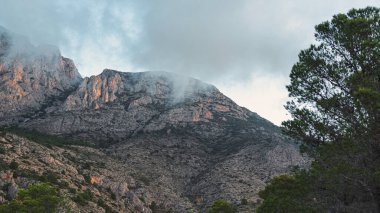 İspanya 'daki Puig Campana' nın engebeli yamaçlarında karamsar bulutlar sürükleniyor, bu ikonik Akdeniz dağ manzarasının dingin güzelliğini ve vahşi atmosferini yakalıyor..
