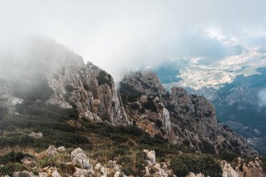 İspanya 'nın Puig Campana bölgesinde engebeli kayalık tepeler ve yeşil yamaçlar üzerinde sürüklenen puslu bulutlar, doğa için dramatik ve atmosferik bir dağ manzarası yaratıyor..