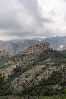 İspanya 'nın engebeli Puig Campana bölgesinin üzerinde karamsar bulutlar süzülüyor, kayalık tepeleri ve yemyeşil ormanı vurguluyor, doğa, seyahat ve macera temaları için mükemmel..