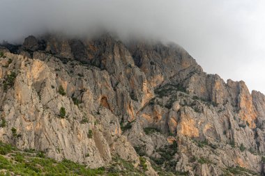İspanya 'daki Puig Campana' nın sarp kayalıkları kalın alçak bulutlara yükselir ve doğa, seyahat ve macera temaları için ideal dramatik ve karamsar bir dağ manzarası yaratır..