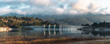 Güney İspanya 'da yemyeşil tepeler ve dramatik bulutlarla çevrili bir baraj ve rezervuarın panoramik görüntüsü, seyahat, doğa ve çevre temaları için ideal.