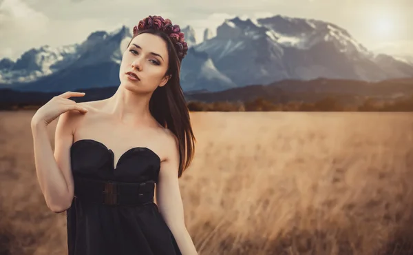 Belle fille dans une robe noire avec des fleurs près des montagnes — Photo