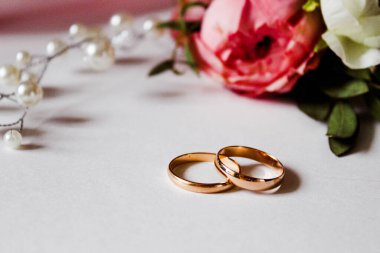 Pembe çiçekler, inci mücevherler ve beyaz arka planda iki altın alyans. Düğün konsepti. İzole edilmiş