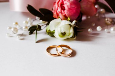 Pembe çiçekler, inci mücevherler ve beyaz arka planda iki altın alyans. Düğün konsepti. İzole edilmiş