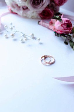 Pembe çiçekler, inci mücevherler ve beyaz arka planda iki altın alyans. Düğün konsepti. İzole edilmiş