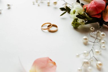 Pembe çiçekler, inci mücevherler ve beyaz arka planda iki altın alyans. Düğün konsepti. İzole edilmiş