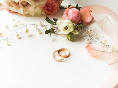 Pembe çiçekler, inci mücevherler ve beyaz arka planda iki altın alyans. Düğün konsepti. İzole edilmiş