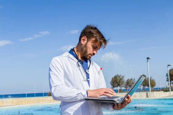 Male young doctor using laptop outdoors.