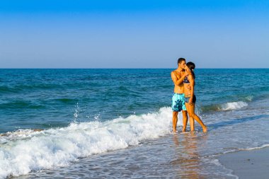 Bronzlaşmış, güzel insanlar. Mutlu genç çift, atletik zayıf vücut, yaz tatili boyunca tropikal plajda öpüşmenin keyfini çıkar..