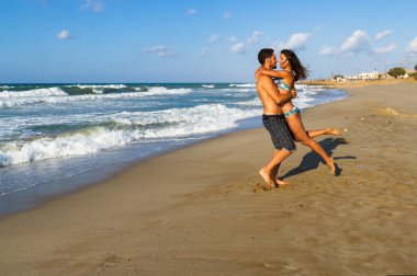 Bikinili, şortlu, kumsalda eğlenen genç bir çift..