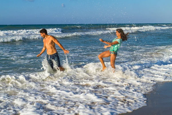 Speels jong stel in bikini en korte broek, plagen elkaar op het strand. — Stockfoto