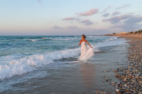 Young bride enjoys a lonesome walk on the beach at dusk — Stock Photo, Image