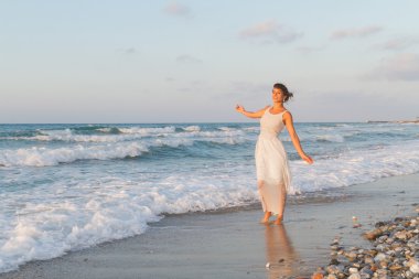 Young woman enjoys a lonesome walk on the beach at dusk.