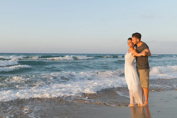 Pareja joven disfruta caminando en una playa nebulosa al atardecer . — Foto de Stock