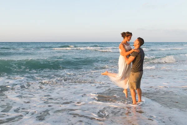 Jovem casal gosta de caminhar em uma praia nebulosa ao entardecer . — Fotografia de Stock