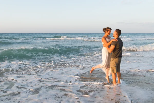 Pareja joven disfruta caminando en una playa nebulosa al atardecer . — Foto de Stock