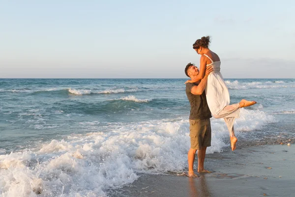Jovem casal gosta de caminhar em uma praia nebulosa ao entardecer . — Fotografia de Stock
