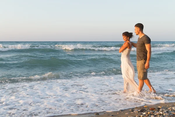 Giovane coppia gode di camminare su una spiaggia nebbiosa al tramonto . — Foto Stock