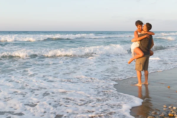 Giovane coppia gode di camminare su una spiaggia nebbiosa al tramonto . — Foto Stock