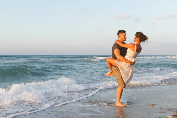 Giovane coppia gode di camminare su una spiaggia nebbiosa al tramonto . — Foto Stock