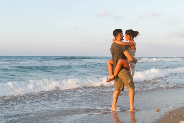 Giovane coppia gode di camminare su una spiaggia nebbiosa al tramonto . — Foto Stock