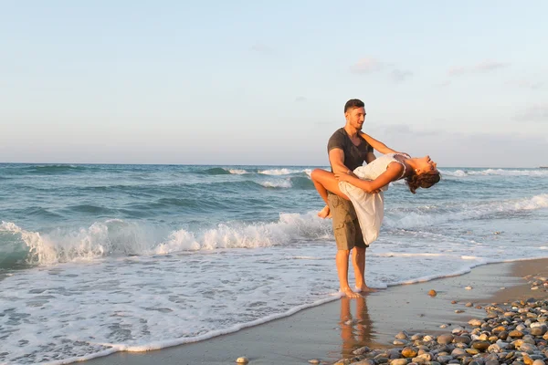 Jovem casal gosta de caminhar em uma praia nebulosa ao entardecer . — Fotografia de Stock