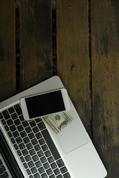 Laptop smartphone och dollarn på trä bakgrund — Stockfoto