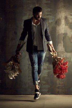 Yakışıklı delikanlı buket çiçek ile akıllı ceketli duvarın önünde poz veriyor.