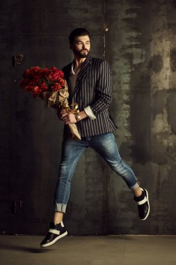 Yakışıklı delikanlı buket çiçek ile akıllı ceketli duvarın önünde poz veriyor.
