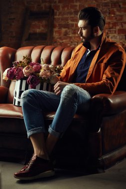 Yakışıklı delikanlı buket çiçek ile akıllı ceketli duvarın önünde poz veriyor.