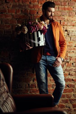 Yakışıklı delikanlı buket çiçek ile akıllı ceketli duvarın önünde poz veriyor.