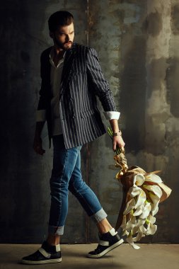 Yakışıklı delikanlı buket çiçek ile akıllı ceketli duvarın önünde poz veriyor.